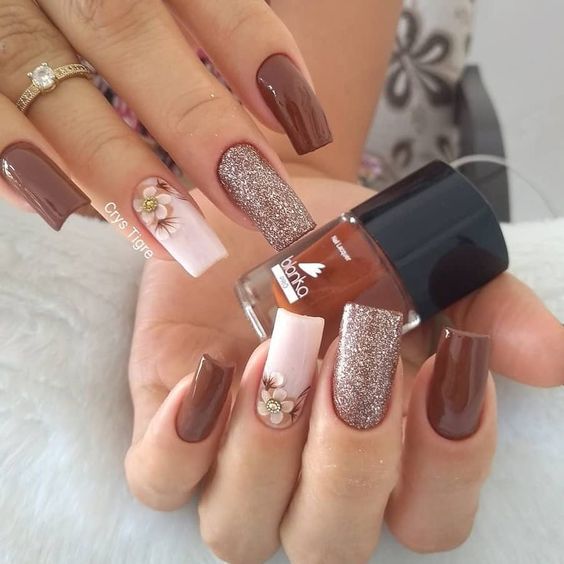 Imagem com unhas marrons decoradas com flor e glitter