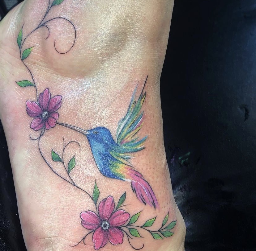 Imagem com tatuagem de flor no pé colorida com beija-flor