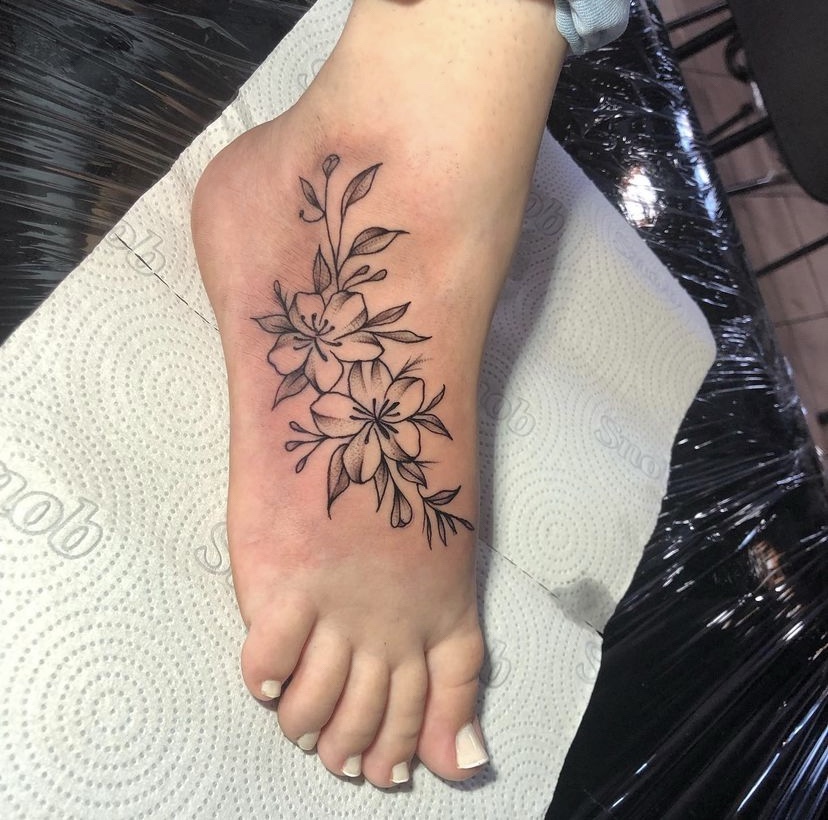 Imagem com tatuagem de flor no pé com traço fino