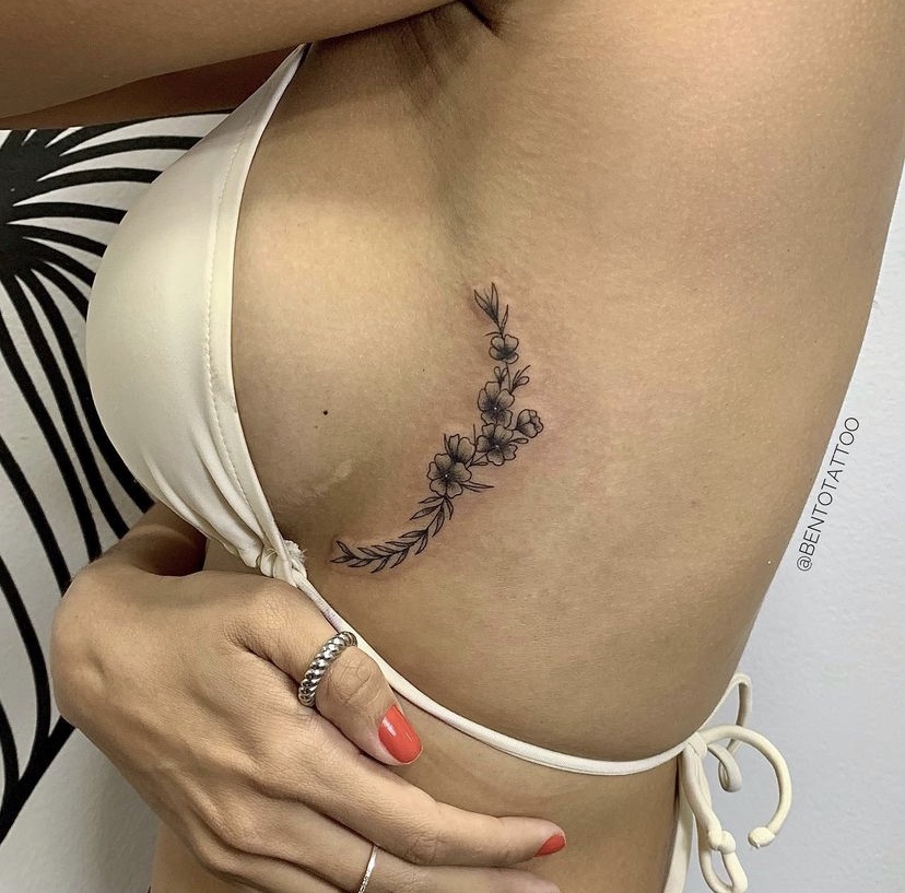 Imagem com tatuagem de ramo com flor na lateral do corpo